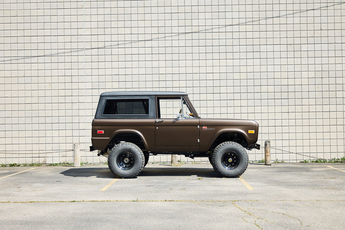 Brown Classic Ford Bronco with black hardtop, lifted suspension, and rugged off-road tires shown in clean side profile, highlighting vintage 4x4 design and restored craftsmanship.