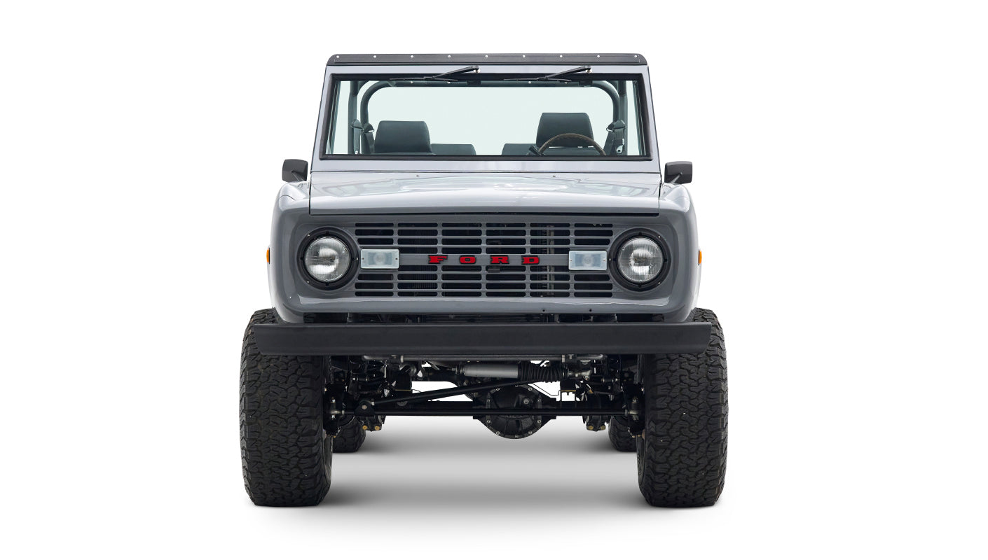 Front view of a Classic Ford Bronco in gray with a black grille, round headlights, and large tires