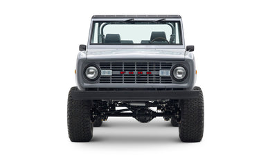 Front view of a Classic Ford Bronco in gray with a black grille, round headlights, and large tires