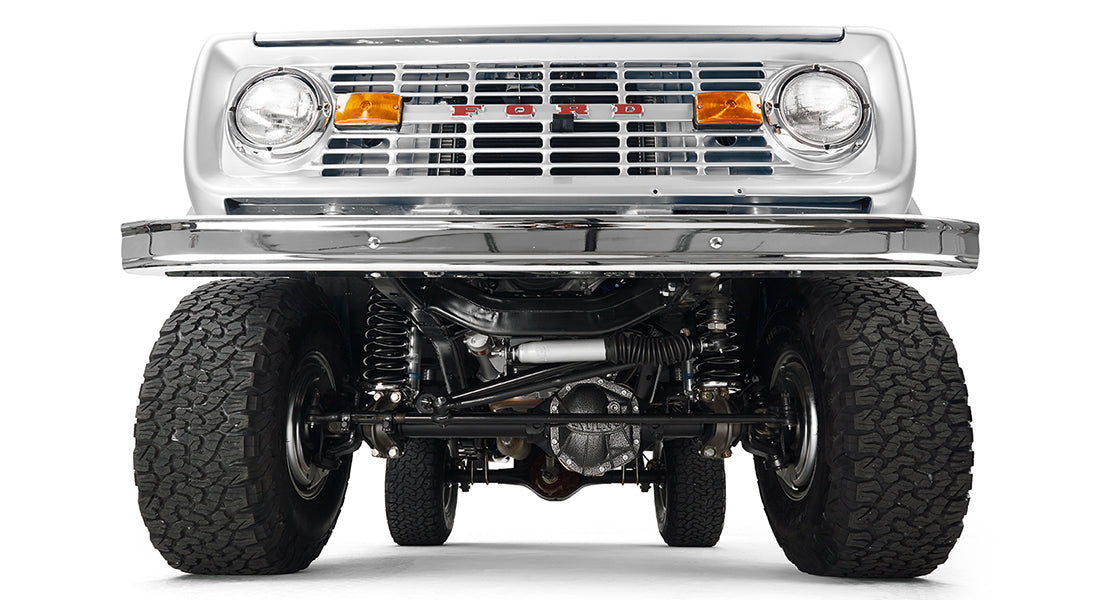 Silver Classic Ford Bronco front suspension and undercarriage view with tires and grille.