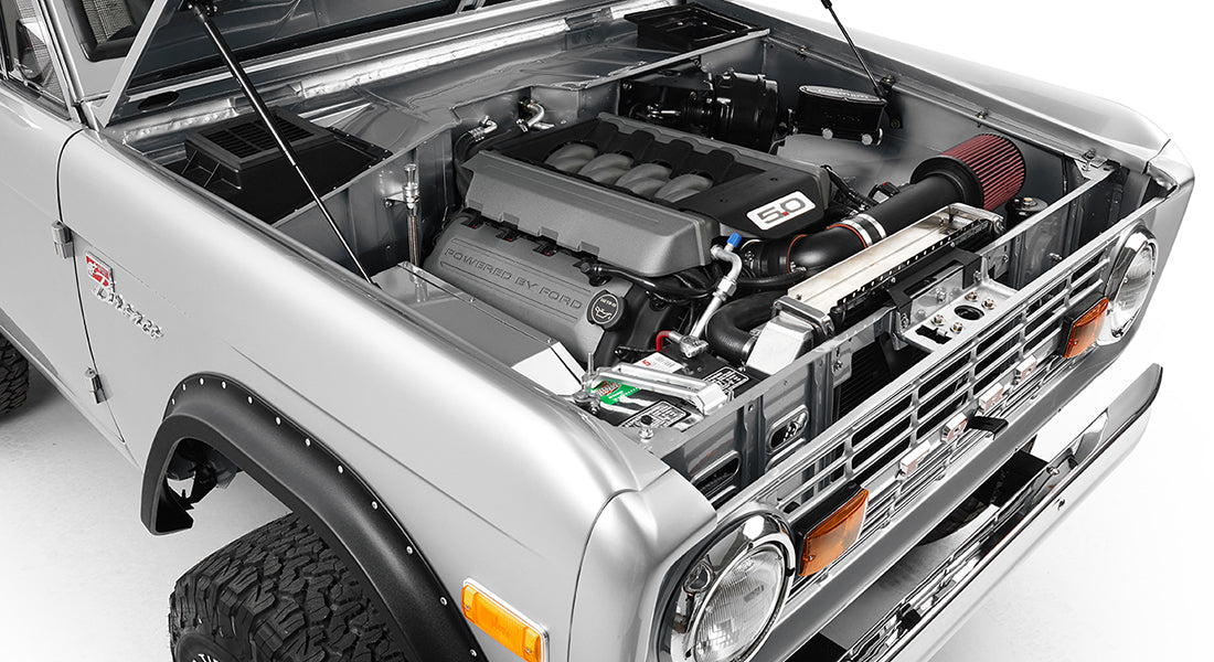 Open hood showing a 5.0 liter engine inside silver Classic Ford Bronco