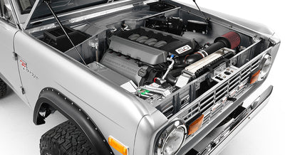 Open hood showing a 5.0 liter engine inside silver Classic Ford Bronco