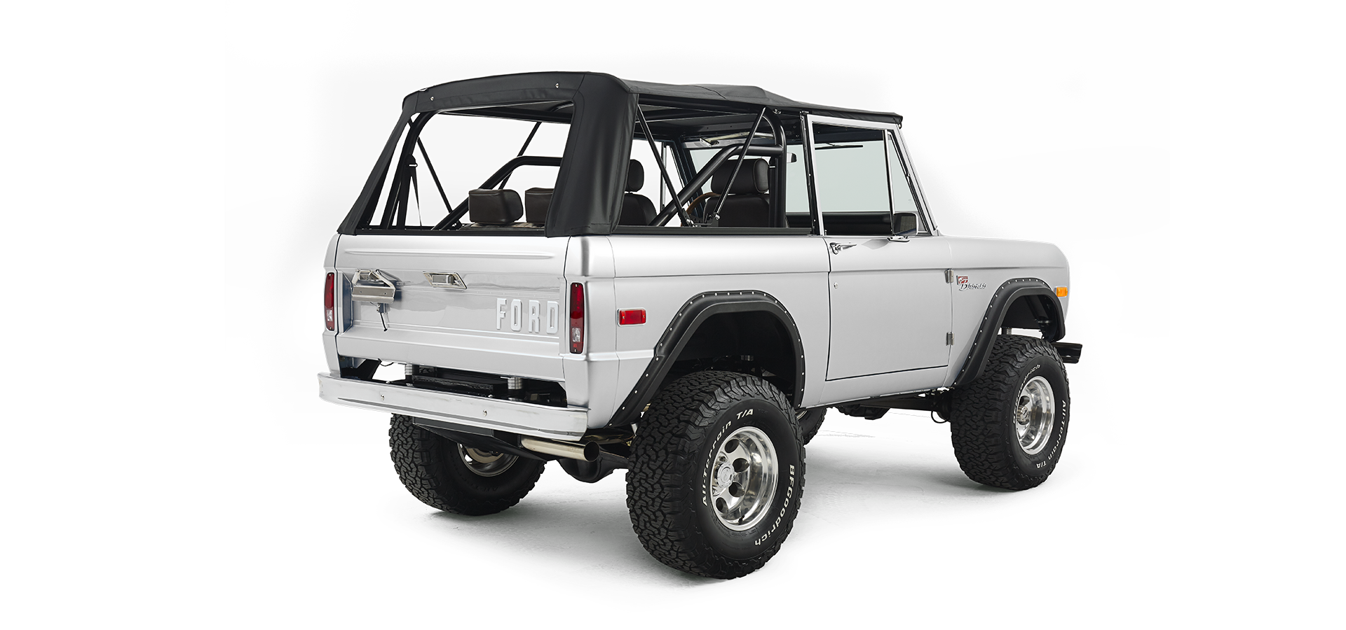 Rear three-quarter view of silver Classic Ford Bronco with black soft top and visible exhaust pipe