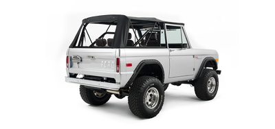 Rear three-quarter view of silver Classic Ford Bronco with black soft top and visible exhaust pipe