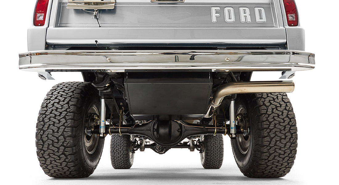 Rear view of silver Classic Ford Bronco showing suspension, exhaust, and FORD tailgate lettering.