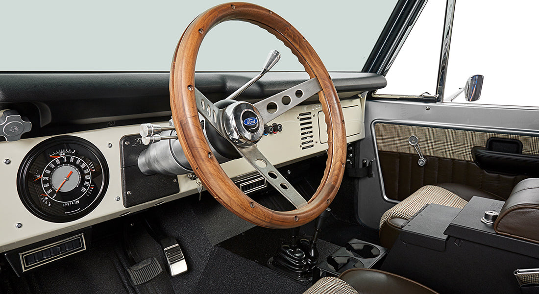 Classic Ford Bronco driver cockpit showing steering wheel, instrument panel, and door interior.