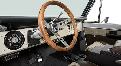 Classic Ford Bronco driver cockpit showing steering wheel, instrument panel, and door interior.