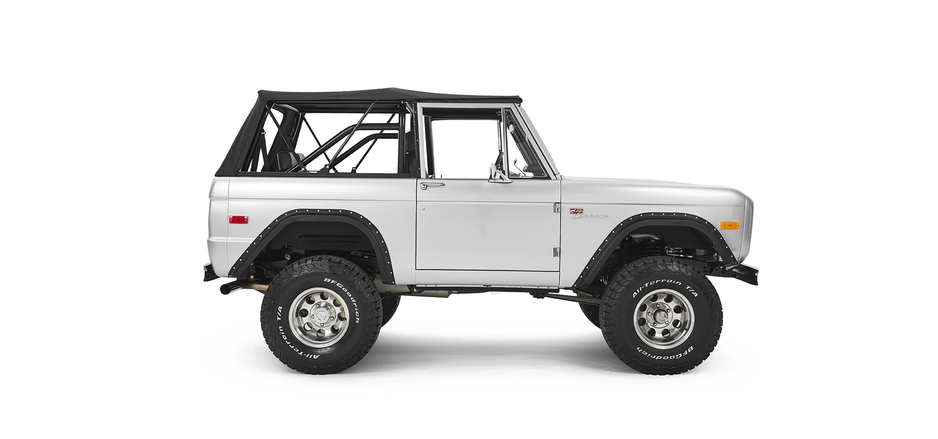 Silver Classic Ford Bronco side profile with black soft top and large off-road tires