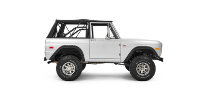Silver Classic Ford Bronco side profile with black soft top and large off-road tires