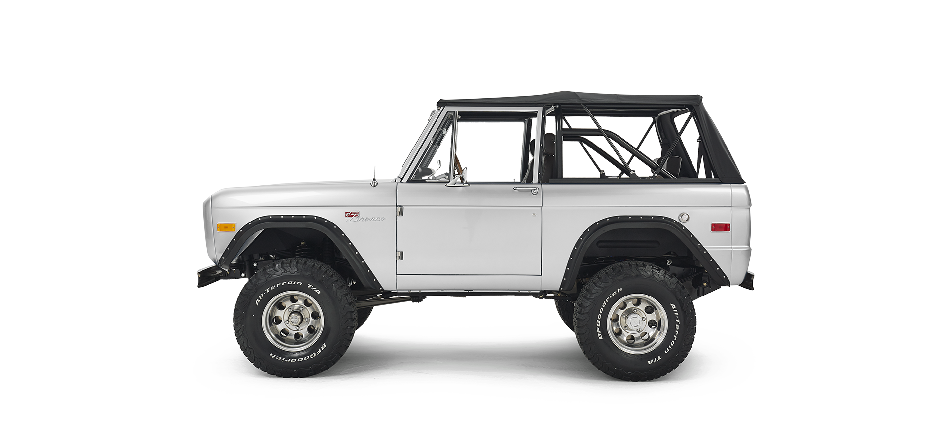 Side view of silver Classic Ford Bronco with black soft top and large off-road tires