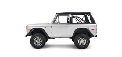 Side view of silver Classic Ford Bronco with black soft top and large off-road tires