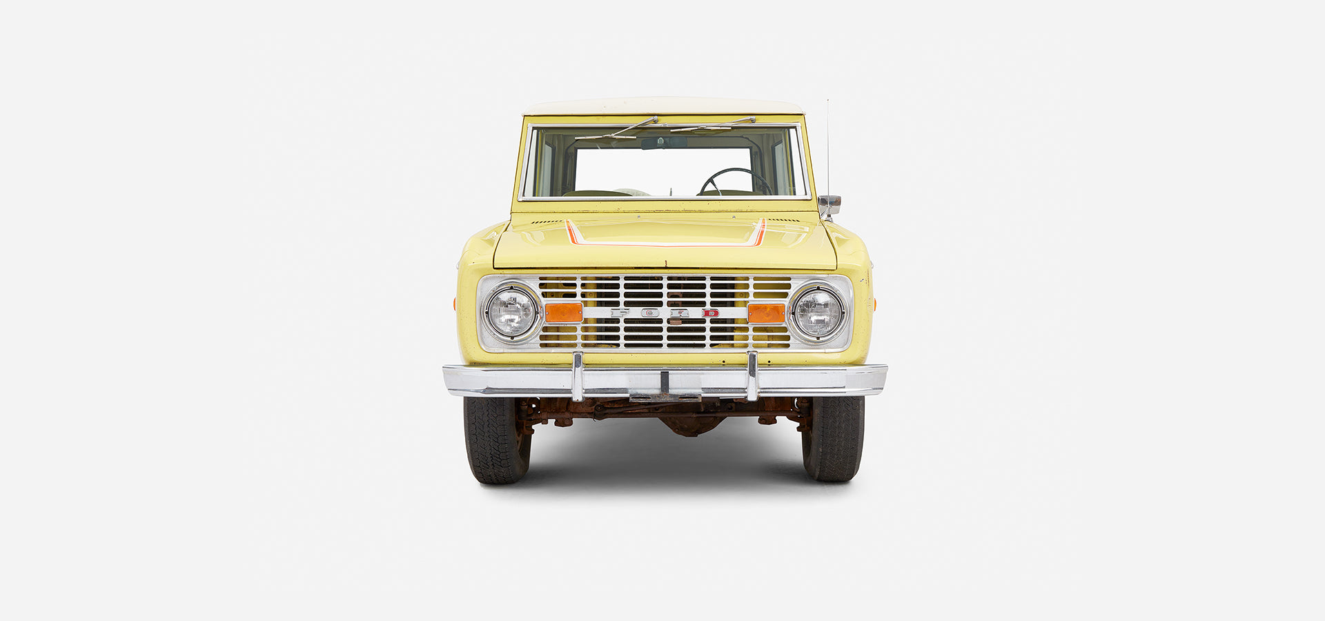 Yellow Classic Ford Bronco front view with white roof and red stripe detailing
