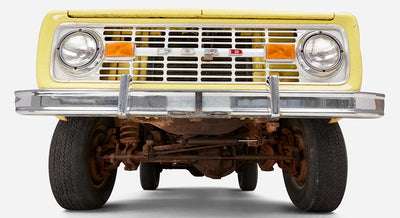 Close-up front view showing grille, headlights, and undercarriage of yellow Classic Ford Bronco