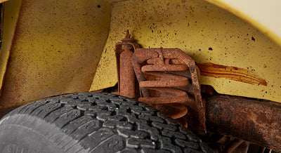 Close-up view of rusted suspension spring and tire inside wheel well of yellow Classic Ford Bronco