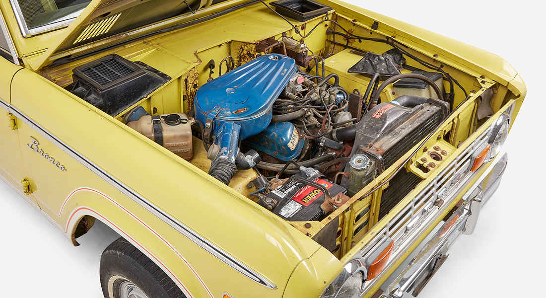 Front side view of Classic Ford Bronco with open hood revealing engine and yellow exterior