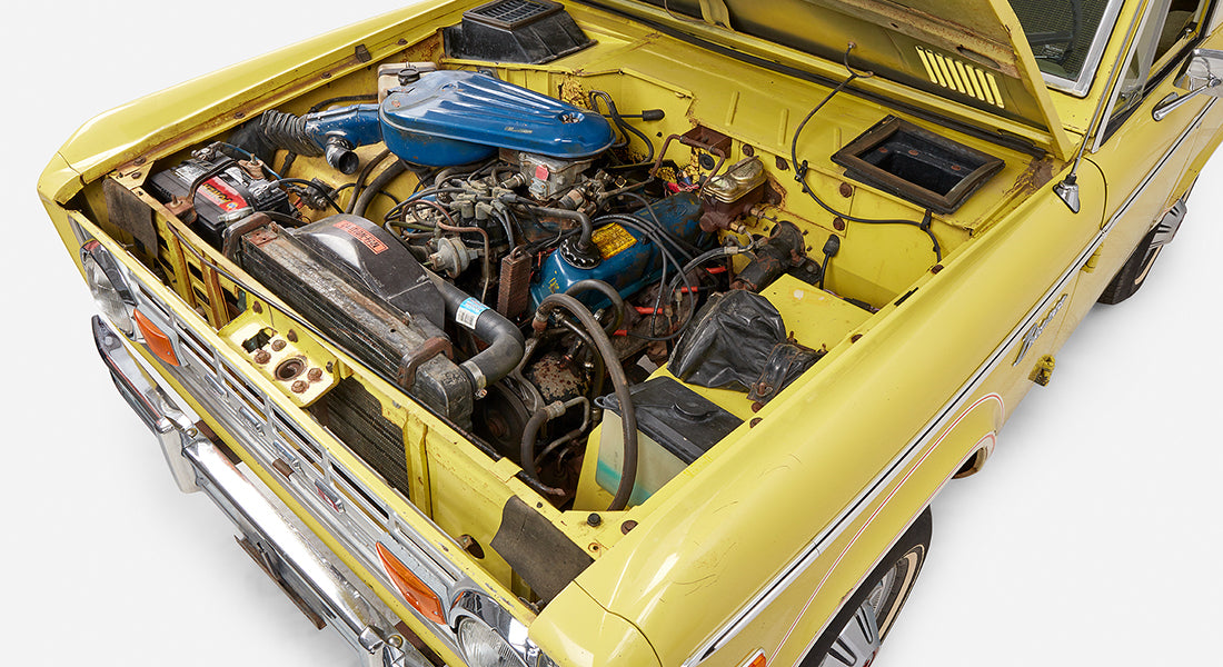 Angled view of engine bay in Classic Ford Bronco with hood open, showing various engine parts and battery