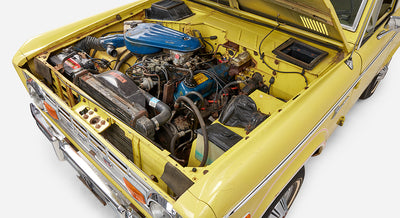 Angled view of engine bay in Classic Ford Bronco with hood open, showing various engine parts and battery