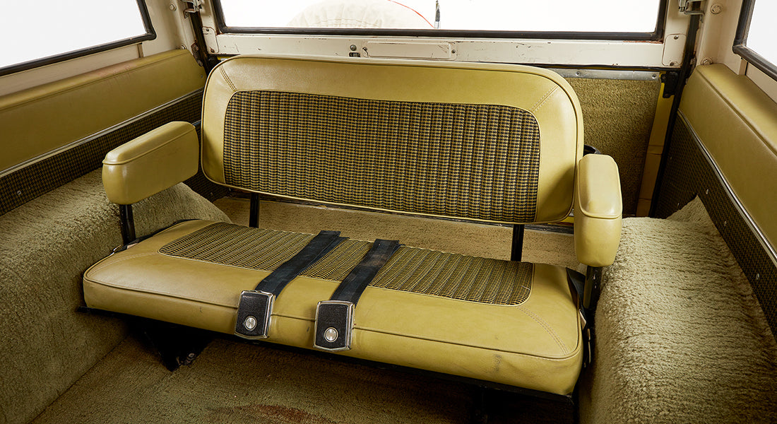Rear interior bench seat of Classic Ford Bronco with yellow and black houndstooth upholstery and seat belts