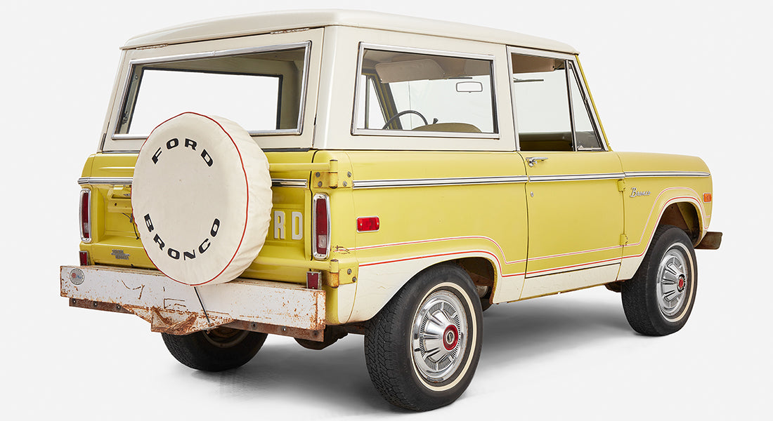 Yellow Classic Ford Bronco angled rear left view showing spare tire and rusted bumper