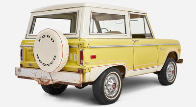 Yellow Classic Ford Bronco angled rear left view showing spare tire and rusted bumper