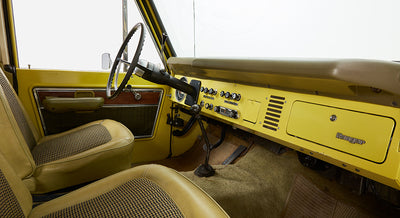 Driver side interior of Classic Ford Bronco featuring yellow dashboard, black steering wheel, and seats