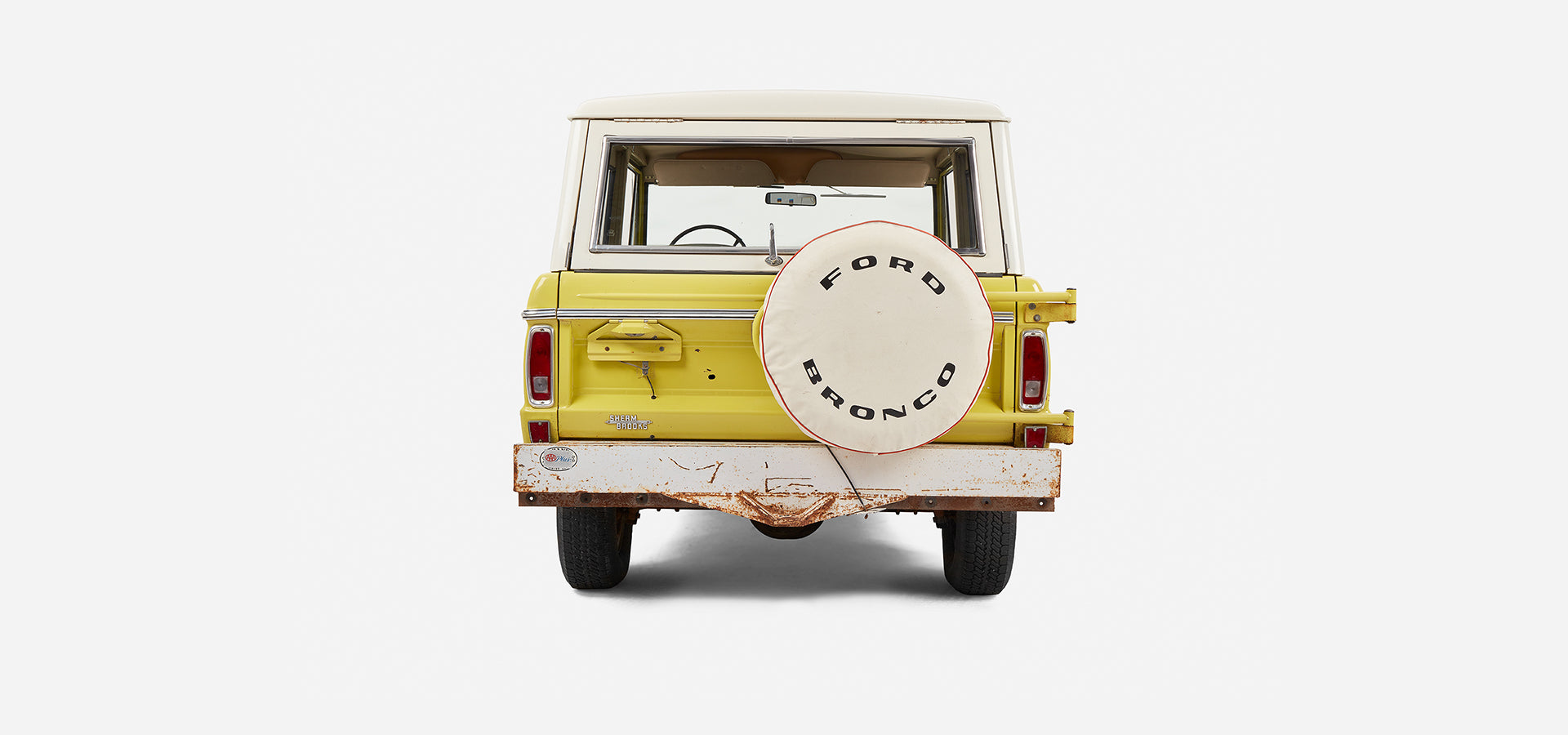 Rear view of yellow Classic Ford Bronco with white spare tire cover and rusted bumper