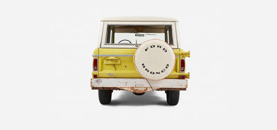 Rear view of yellow Classic Ford Bronco with white spare tire cover and rusted bumper