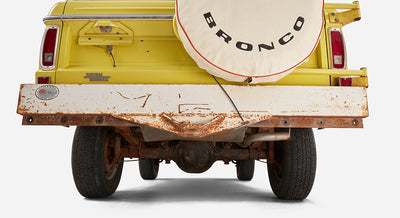 Rear view of yellow Classic Ford Bronco with white spare tire cover and rusted bumper
