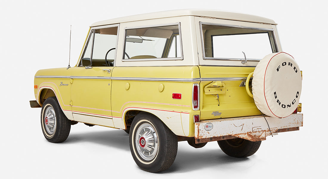 Side and rear angled view of yellow Classic Ford Bronco with white roof and rusted bumper