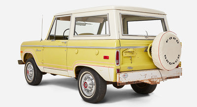 Side and rear angled view of yellow Classic Ford Bronco with white roof and rusted bumper