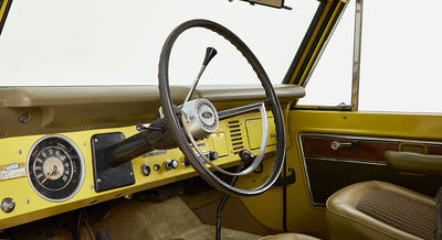 Interior of Classic Ford Bronco showing steering wheel, dashboard, and front seats in yellow and brown
