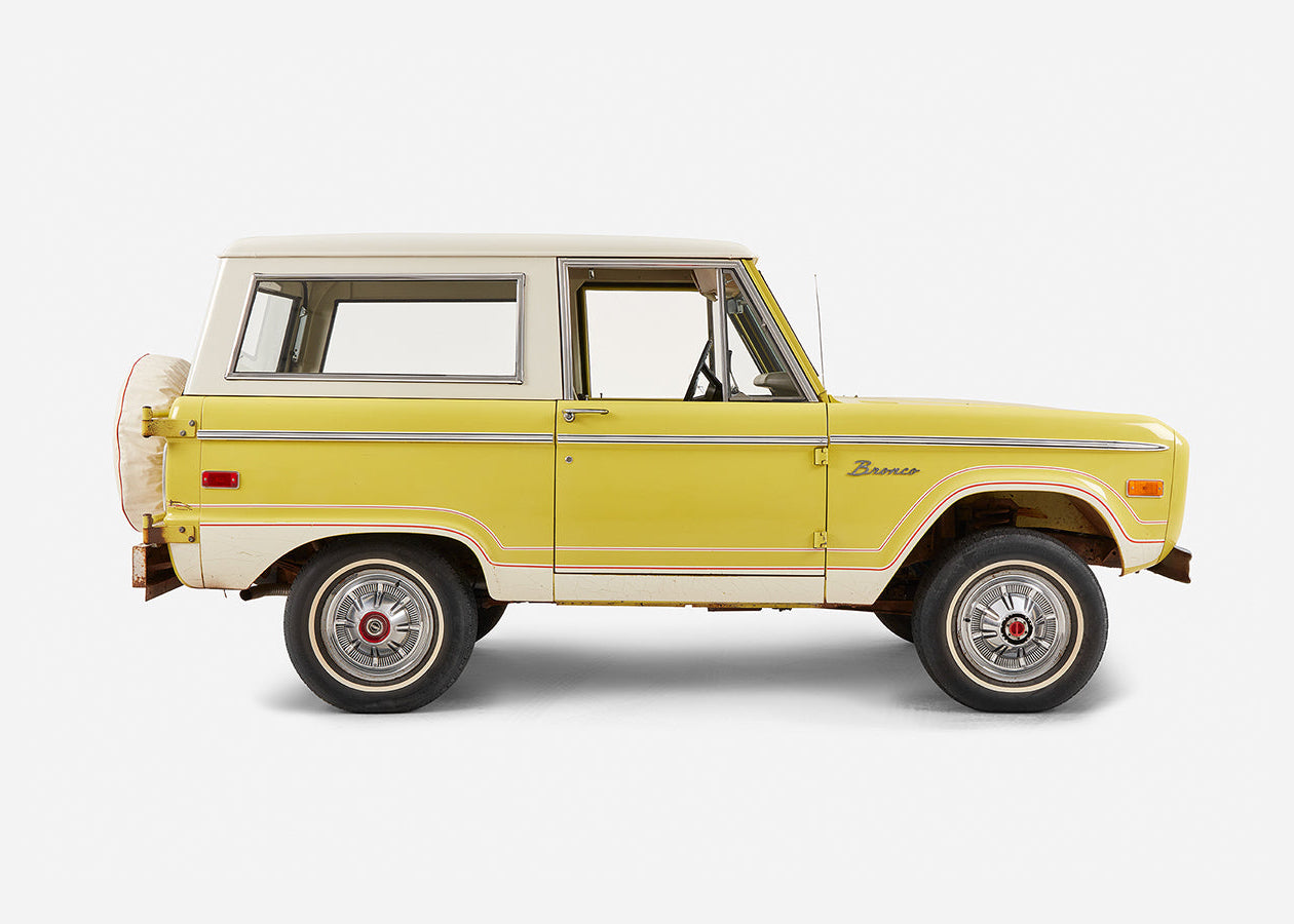 Side profile of yellow Classic Ford Bronco with white roof and full red stripe detail
