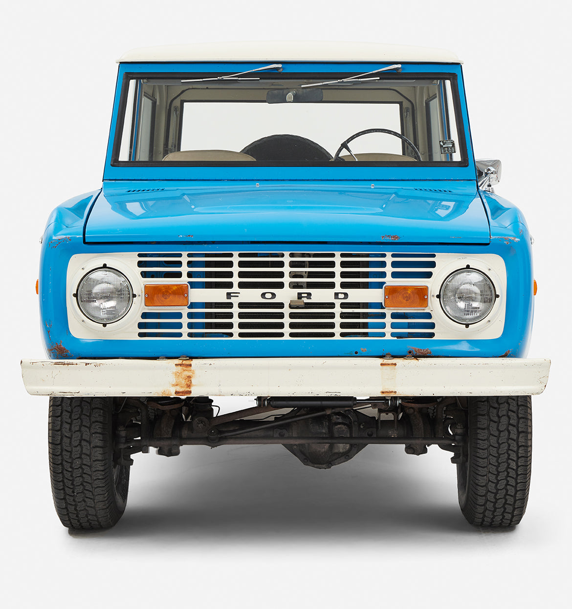 Front view of blue Classic Ford Bronco showing grille, headlights, and white bumper with rust spots