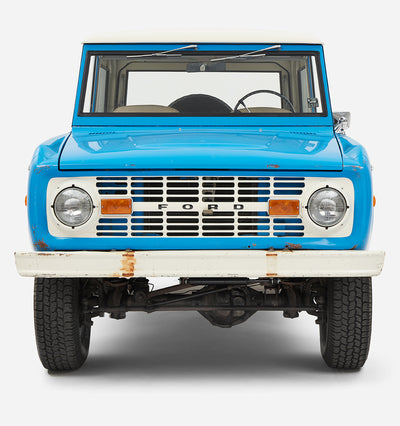 Front view of blue Classic Ford Bronco showing grille, headlights, and white bumper with rust spots