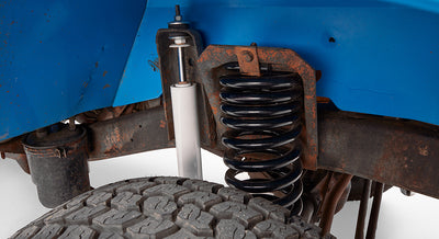 Close-up of suspension coil and white shock absorber next to a blue painted vehicle body panel