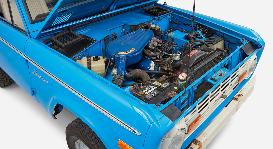 Classic Ford Bronco with open hood displaying engine bay and blue body with white roof