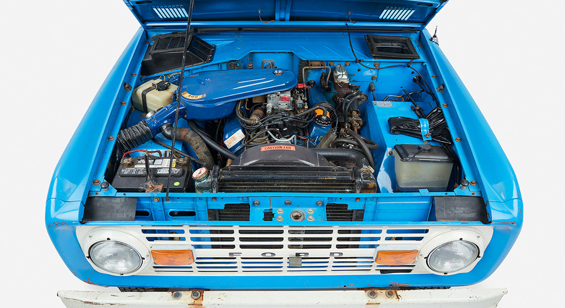 Classic Ford Bronco engine bay viewed from the front with radiator, battery, and engine components