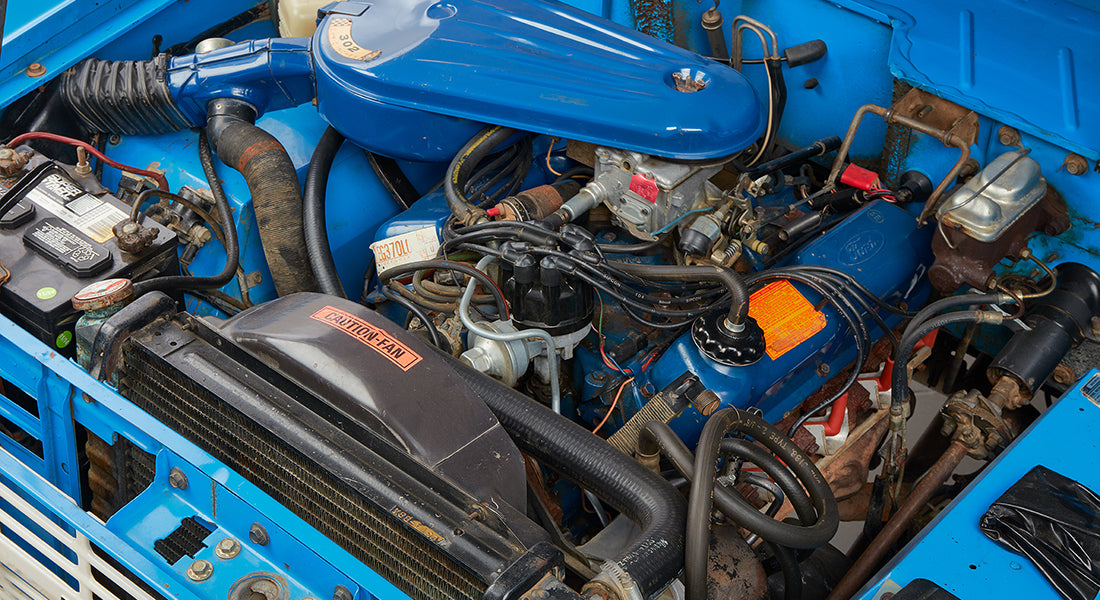Close-up engine details inside Classic Ford Bronco including hoses, battery, and air filter assembly
