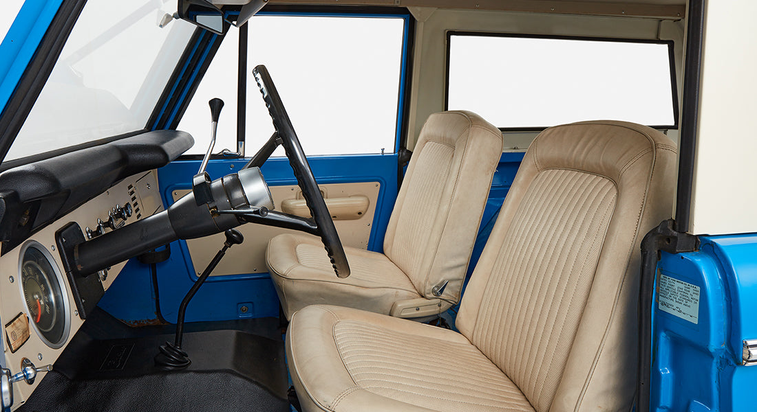 Front interior of Classic Ford Bronco showing beige driver and passenger seats, black steering wheel and dashboard