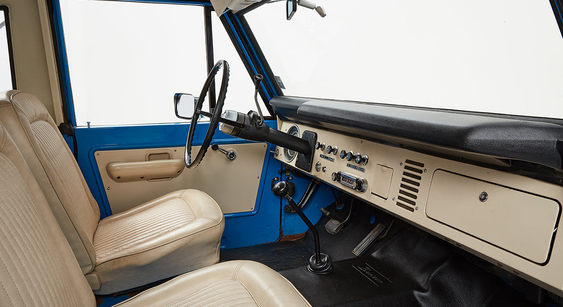 Classic Ford Bronco interior with beige seats, black steering wheel, and blue door panel