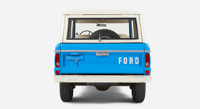 Rear view of Classic Ford Bronco in blue with white roof and a mounted spare tire inside