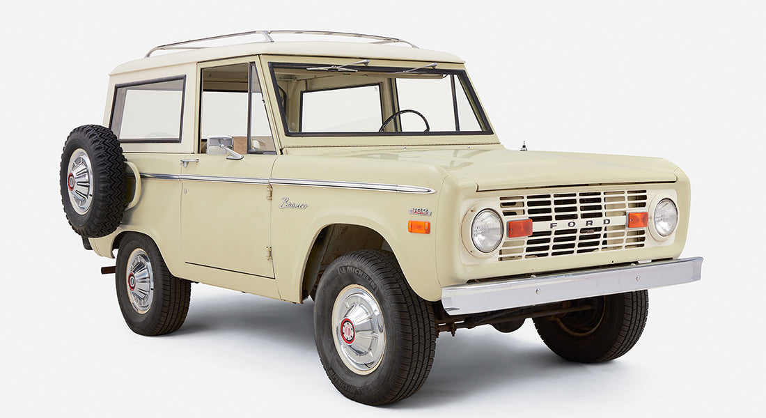 Front side view of a pale yellow Classic Ford Bronco with white roof and chrome wheel hubcaps