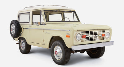 Front side view of a pale yellow Classic Ford Bronco with white roof and chrome wheel hubcaps