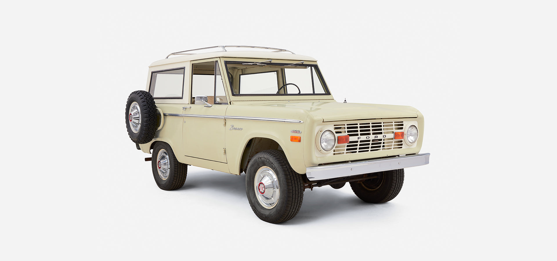 Front three-quarter view of Classic Ford Bronco with white cab, sage body, and spare tire on back