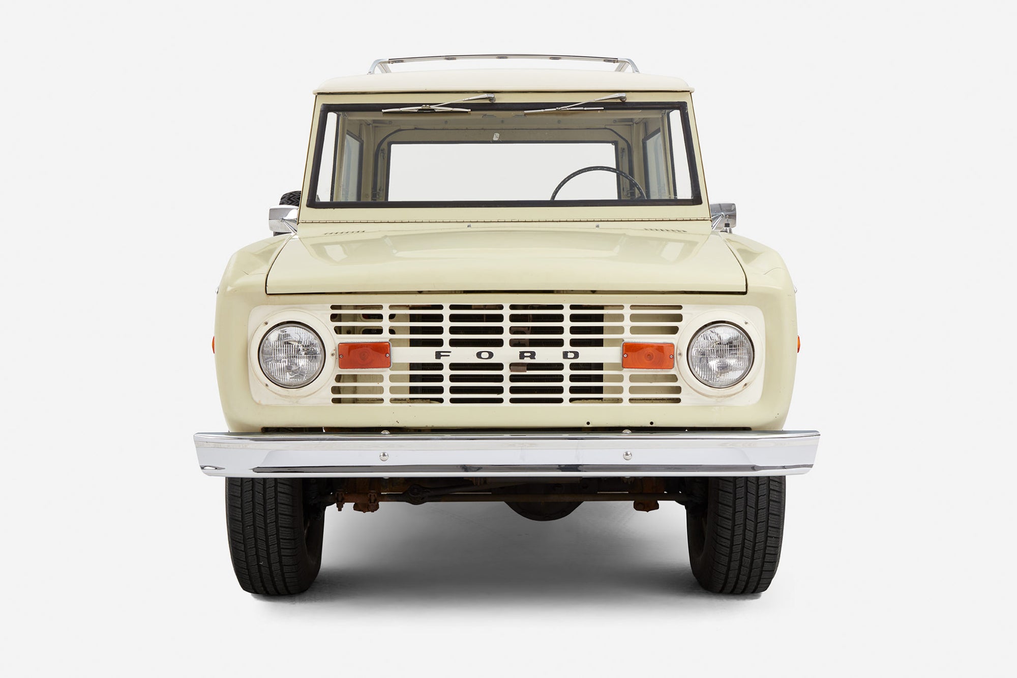 Frontal view of a light yellow Classic Ford Bronco with white roof showing headlights and grille
