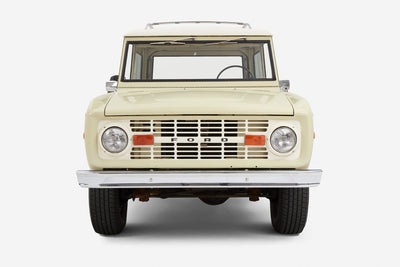 Frontal view of a light yellow Classic Ford Bronco with white roof showing headlights and grille