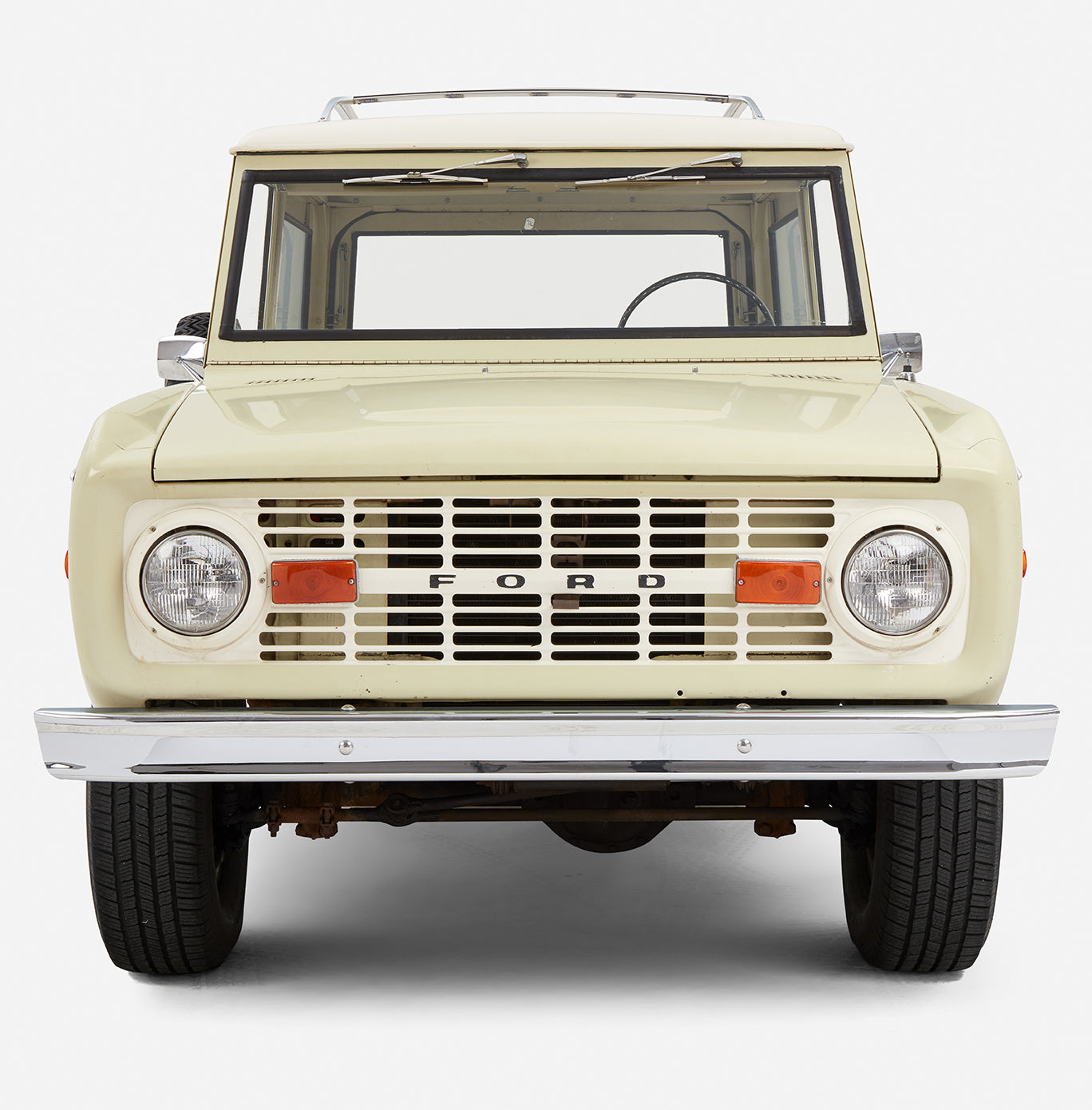 Close-up frontal view of a light yellow Classic Ford Bronco with white roof focusing on grille and headlights