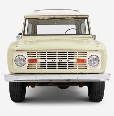 Close-up frontal view of a light yellow Classic Ford Bronco with white roof focusing on grille and headlights
