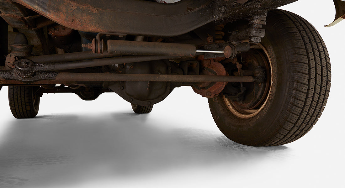 Underside view of a vehicle showing rear axle, leaf springs, and tire on white studio floor
