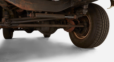 Underside view of a vehicle showing rear axle, leaf springs, and tire on white studio floor